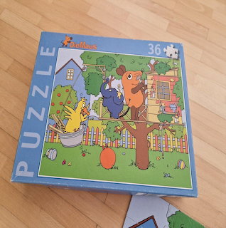 Blue children's puzzle box with cartoon mice illustration lying on a wooden floor
