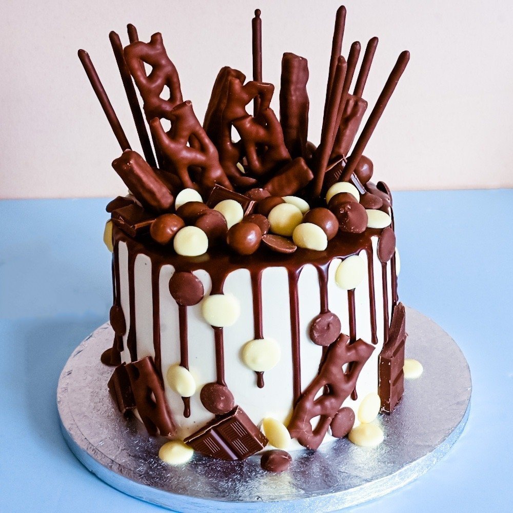 Chocolate drip cake with pretzels, wafer sticks, assorted chocolates, and white chocolate drops