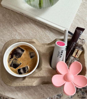 Iced coffee in a white cup on a stone tray with beauty products and a pink flower-shaped accessory