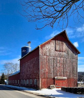 Weathered red barn with blue silo on a sunny winter day with snow on the ground