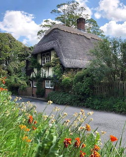 Thatched cottage with half-timbered walls, garden path and blooming flowers in foreground