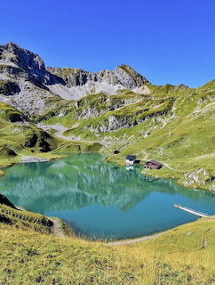 Turquoise alpine lake surrounded by mountains and green meadows with small cabin
