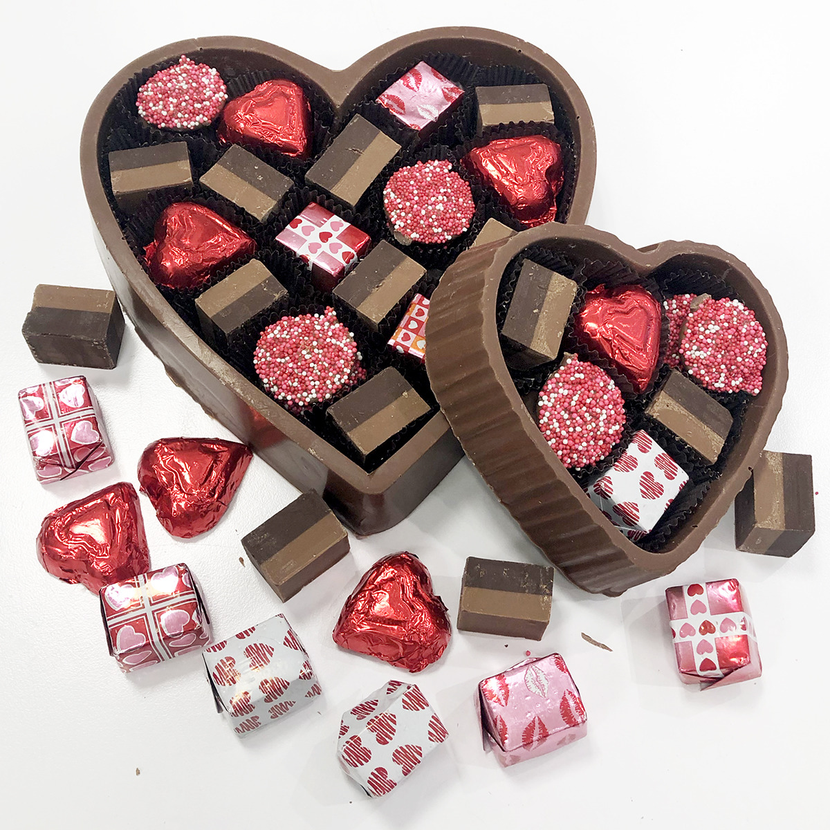 Two heart-shaped chocolate boxes with assorted chocolates and wrapped candies on a white background