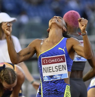 Female track athlete in blue uniform with Nielsen bib celebrating in a stadium