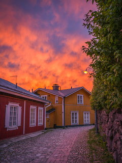 Red and yellow wooden houses on a cobblestone street under a vivid orange sunset sky in Porvoo, Finland