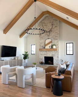 Modern farmhouse living room with vaulted ceiling, wood beams, stone fireplace, white chairs and leather sofa