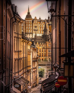 Narrow Stockholm street with historic buildings and a faint rainbow in the cloudy sky
