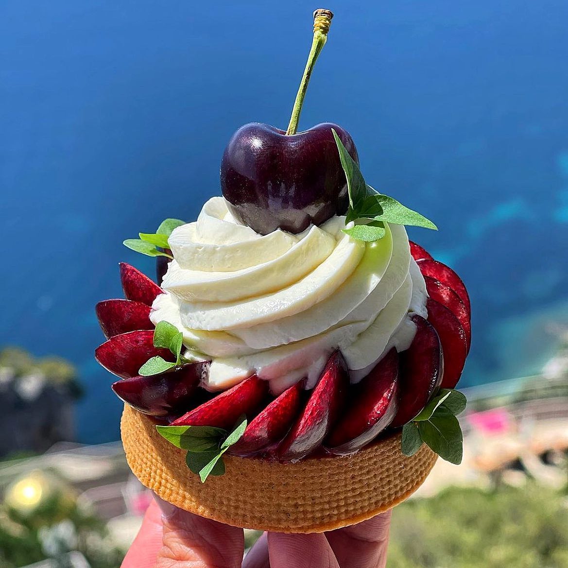 Fruit tartlet with vanilla cream, a dark cherry, and sliced strawberries outdoors