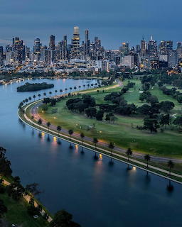 Aerial night view of Melbourne skyline over Albert Park Lake with illuminated roads and green parkland