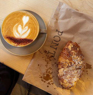 Latte with heart-shaped foam art next to an almond croissant on a wooden table