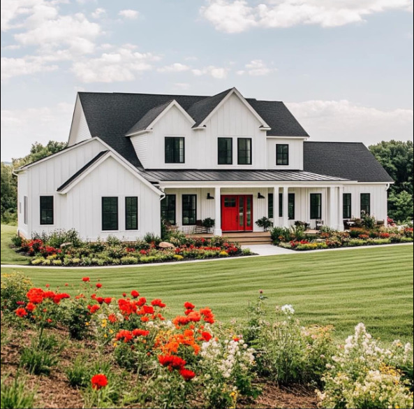 Large white house with a red front door, manicured lawn, and colorful flower beds