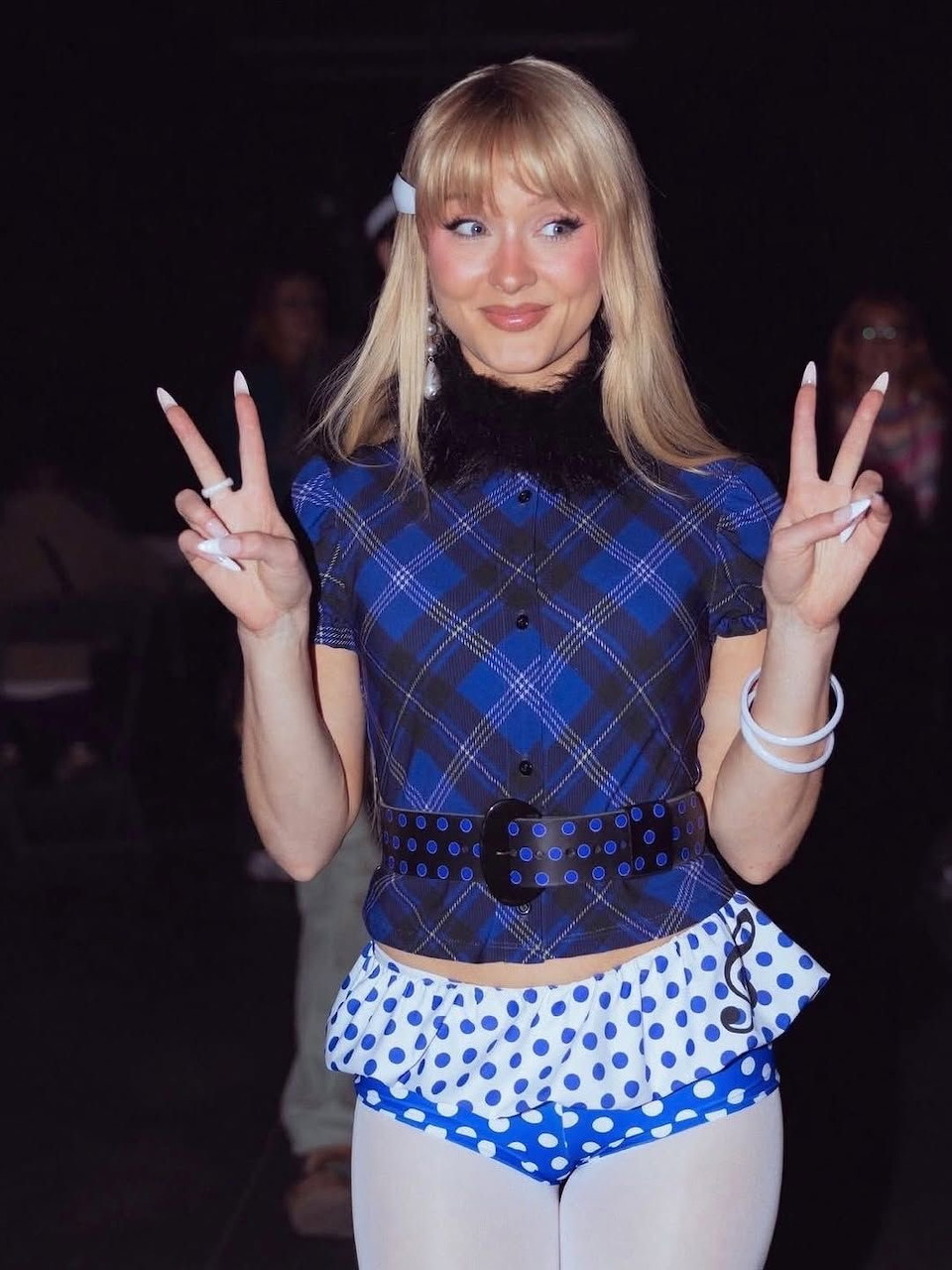 Blonde woman in blue plaid shirt making peace signs with both hands