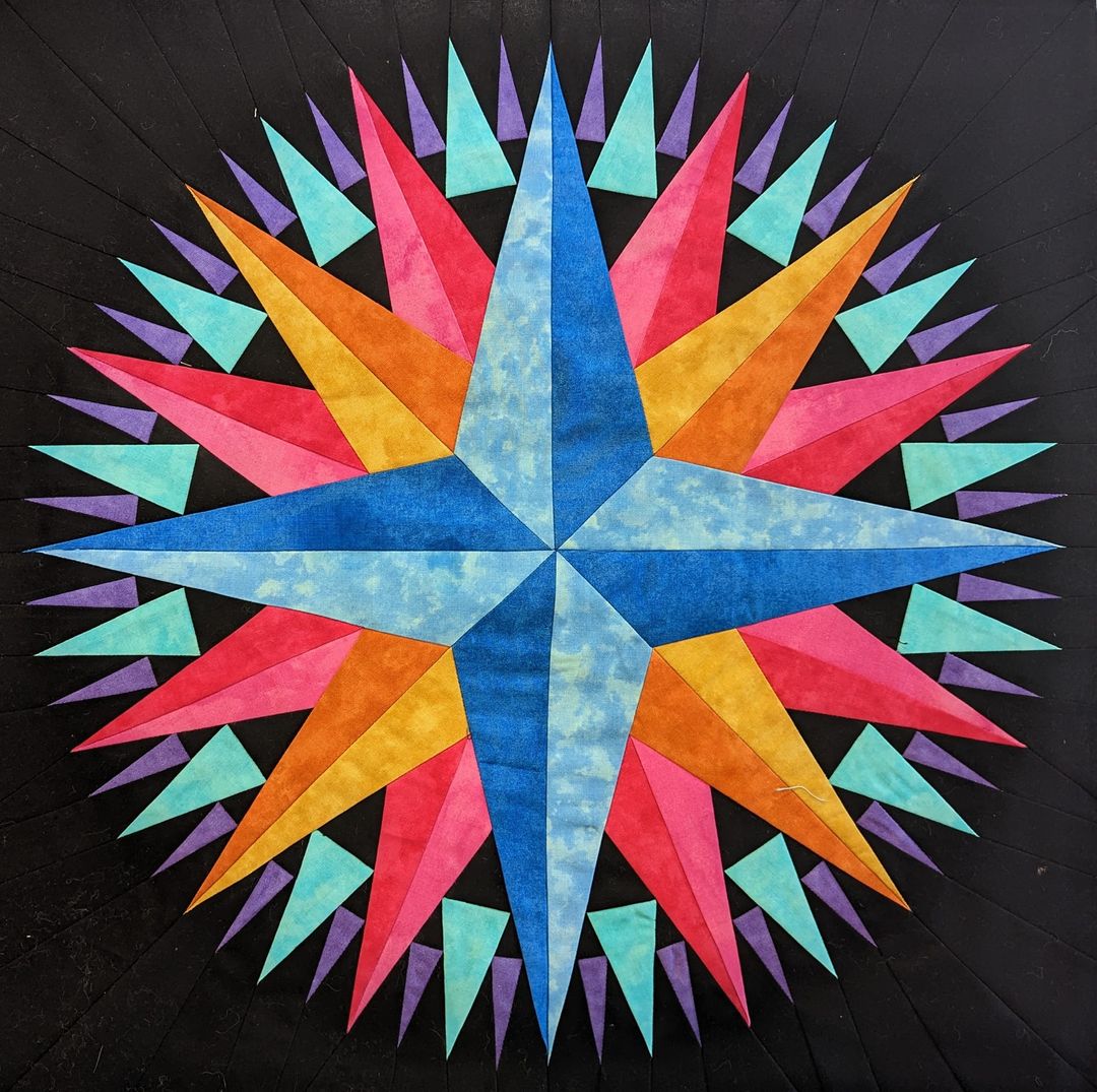 Colorful compass star quilt with geometric radiating points in blue, pink, orange and turquoise fabrics on black background