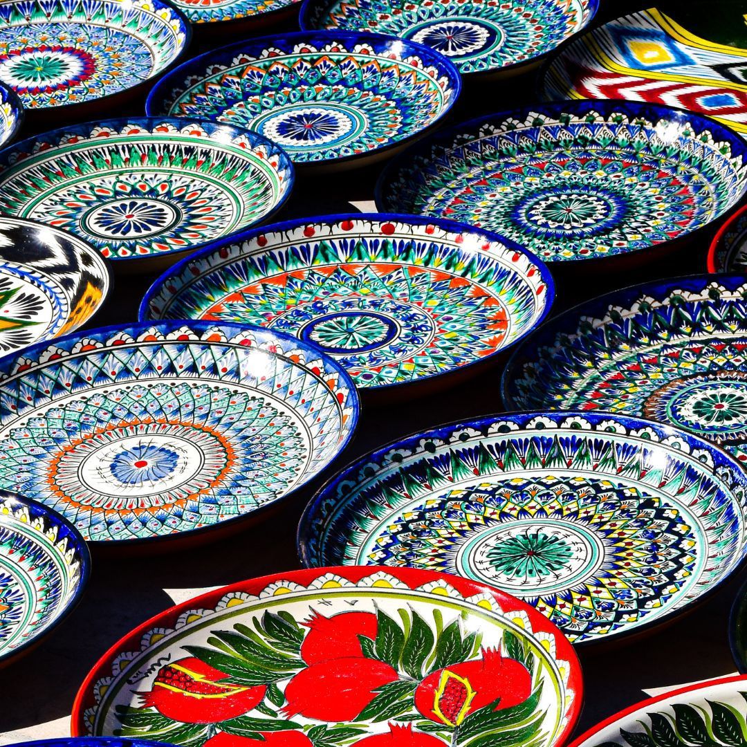 Collection of colorful Uzbek ceramic plates with intricate geometric and floral patterns displayed on black background