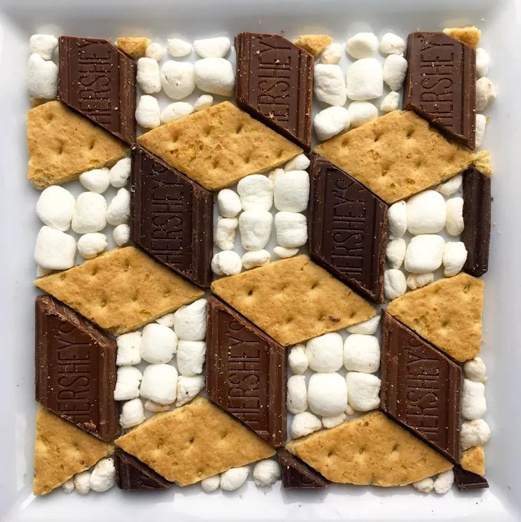 Graham crackers, chocolate pieces, and marshmallows arranged in a 3D cube pattern creating an optical illusion