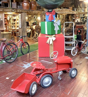 Red toy pedal tractor displayed in antique shop with vintage bicycle and collectibles behind it
