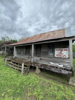 Old weathered wooden cabin with rusty tin roof and front porch in grassy field under stormy sky