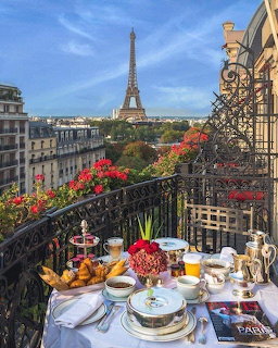 Breakfast table on Parisian balcony with Eiffel Tower in background, flowers, and elegant tableware