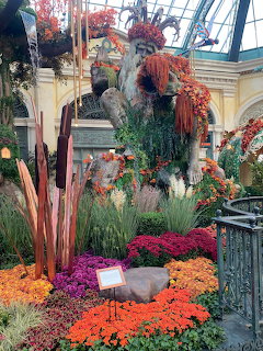 Indoor conservatory with colorful flower beds, ornamental grasses, and planters under glass roof