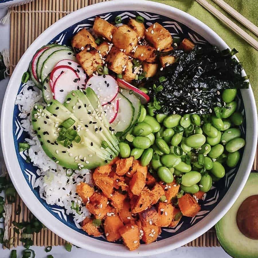 Overhead view of a poke bowl with rice, edamame, avocado, cucumber, radish, nori, and tofu in a blue bowl