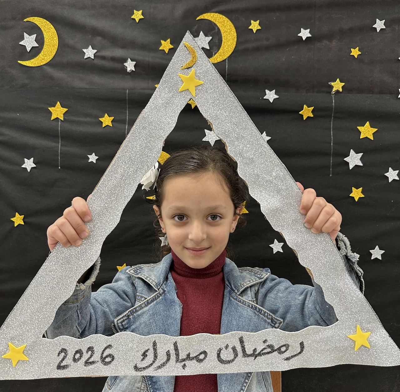 Young girl holding a white Ramadan decoration with stars and crescent moons behind her
