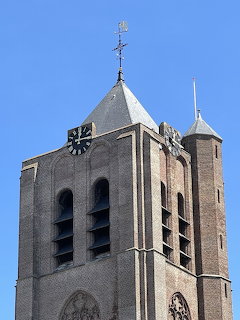 Brick church bell tower with clock, arched windows, and weathervane against blue sky