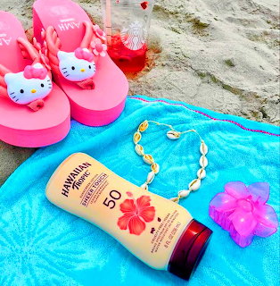 Pink Hello Kitty sandals and sunscreen on blue beach towel with tropical accessories