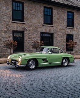 Green Mercedes-Benz 300SL Gullwing classic car parked on cobblestone street in front of stone building