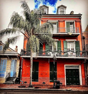 Historic red brick building with decorative iron balconies and palm tree under dramatic cloudy sky