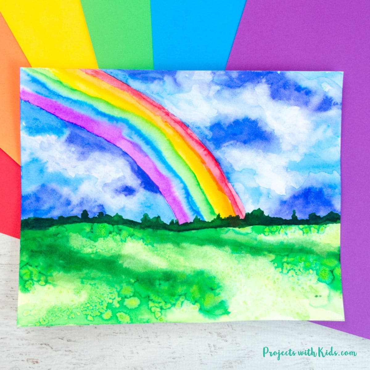 Vibrant rainbow over green landscape with blue sky and clouds, framed by rainbow striped border