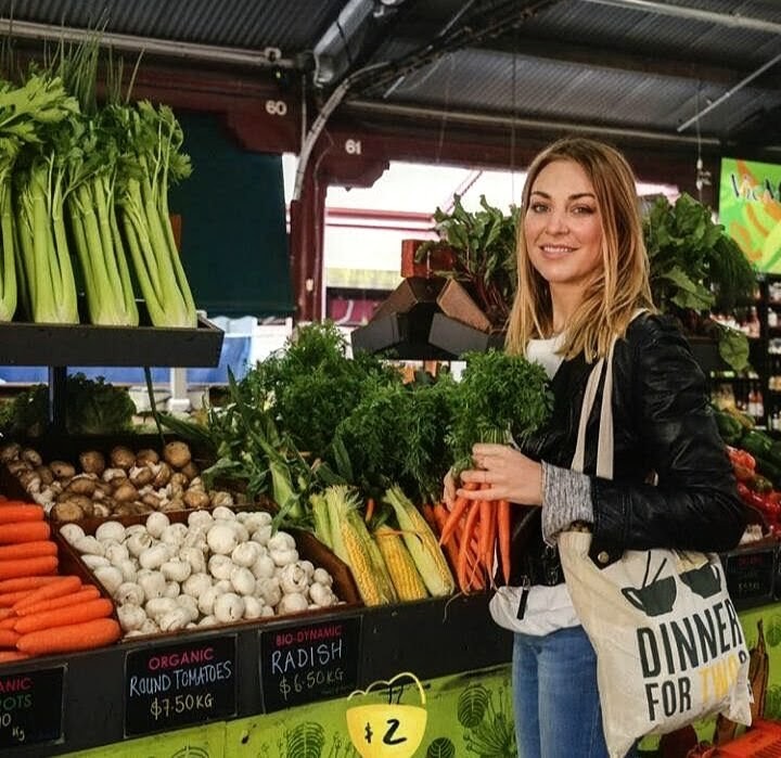 Smiling woman holding carrots at a vegetable market stall with fresh produce
