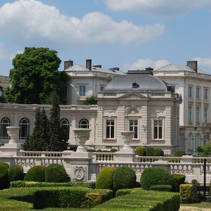 Palace building behind formal hedges and stone balustrades under a blue sky