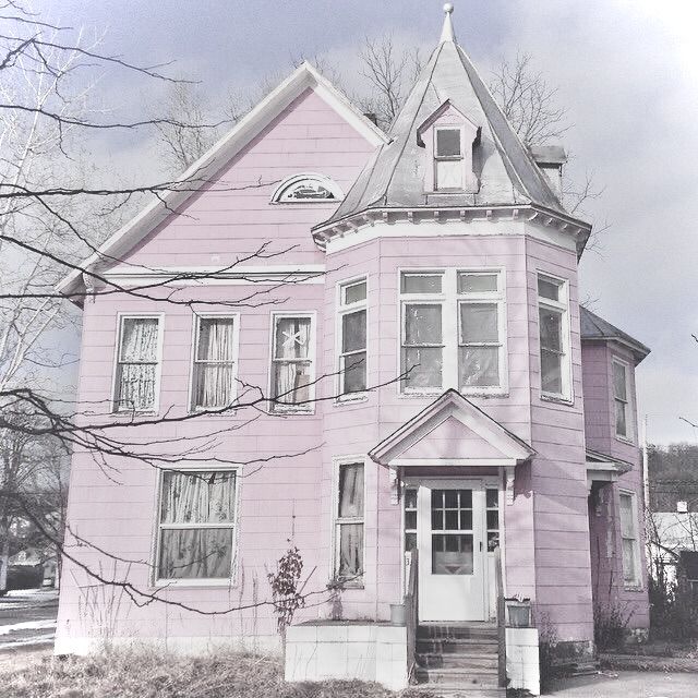 Pale pink Victorian house with a turret, bay windows, and leafless tree branches