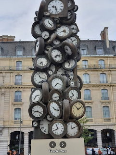 Tall sculpture of stacked vintage clocks in front of a historic building in Paris