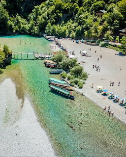 Aerial view of turquoise river beach with boats and people in Albanian valley