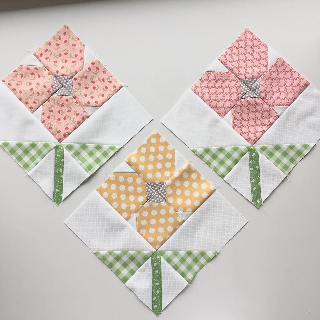 Three quilted flower blocks with patterned fabric petals, green gingham stems, and button centers arranged on white fabric