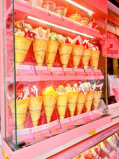 Pink lit display case with multiple rows of ice cream cones and crepes with various toppings