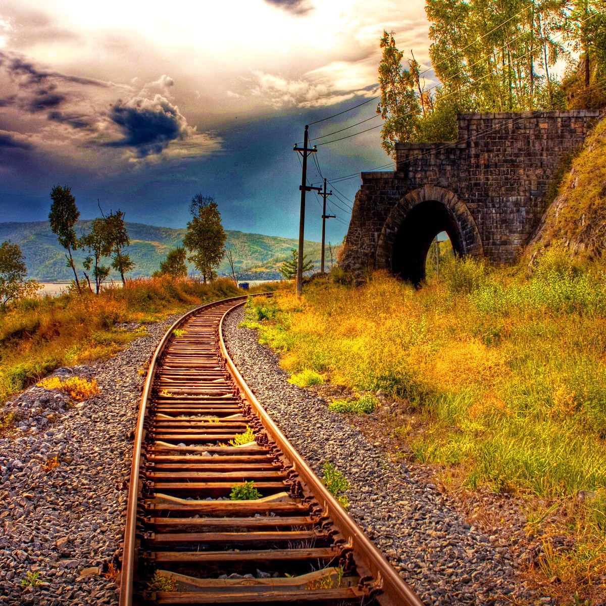 Railway tracks leading to stone tunnel in mountain landscape with dramatic sky