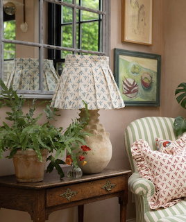 Cottage interior with ceramic lamp, potted plants on rustic table, striped armchair, and framed artwork on wall