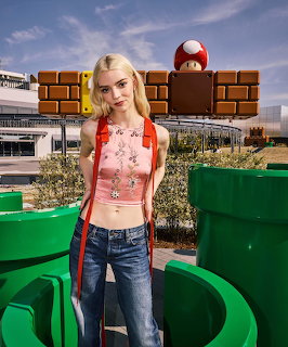 Blonde woman in pink crop top and jeans standing near green pipes and brick blocks at Nintendo theme park