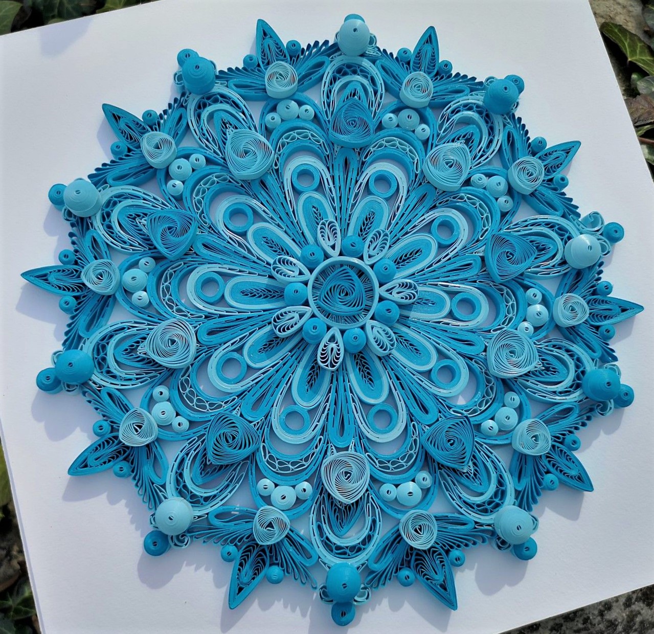 Detailed blue paper quilling mandala with ornate swirling patterns and layered petals in concentric circles