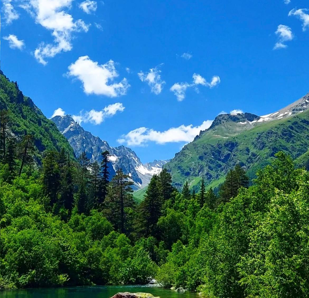Green valley with dense forests, mountain peaks, and blue sky in the Caucasus region