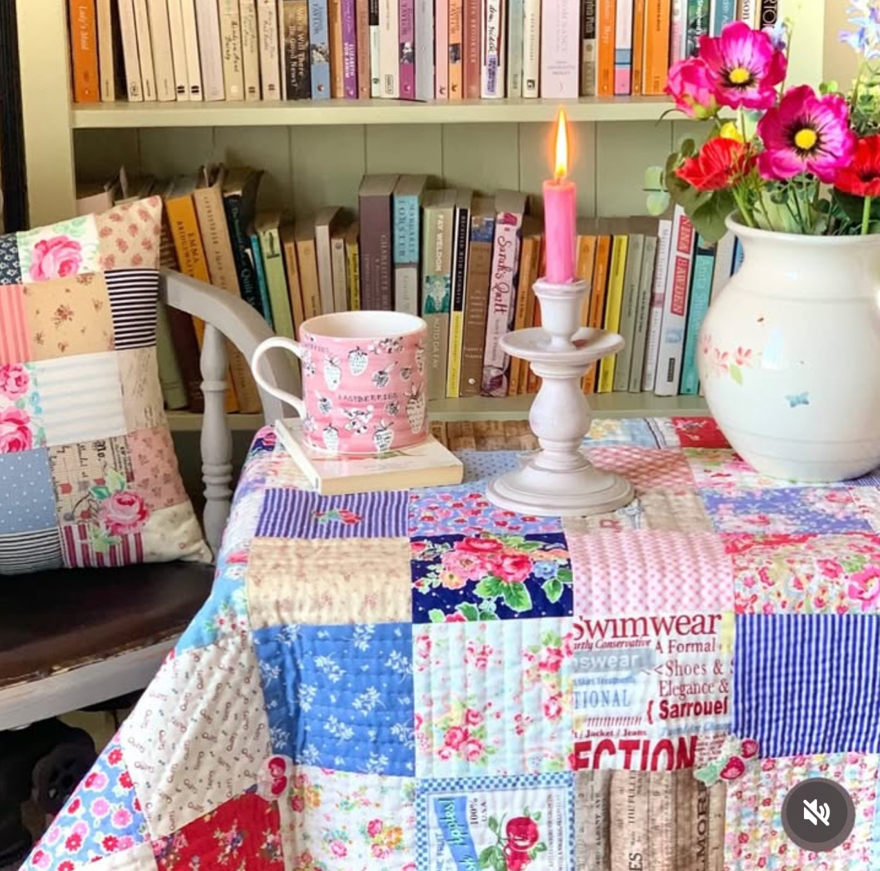 Tea table with patchwork quilt, teacups, flowers in pitcher, and bookshelf background