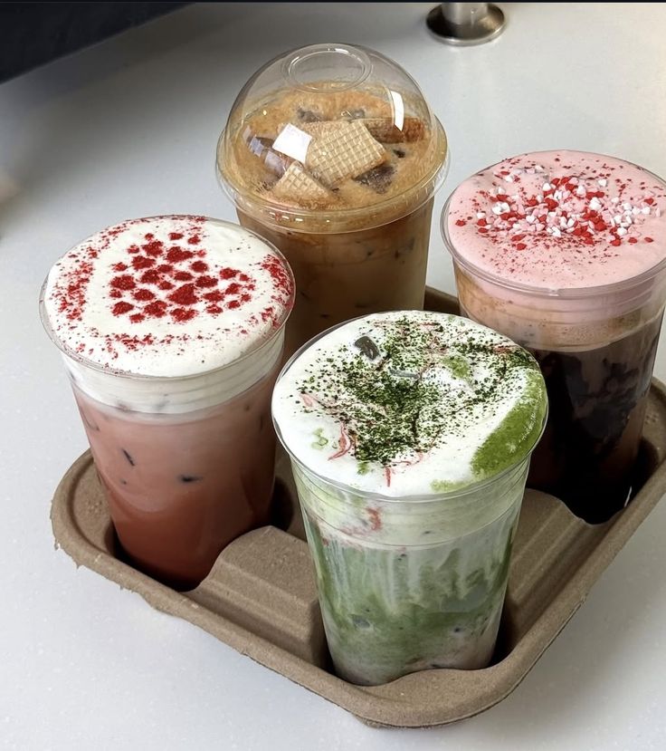 Four iced lattes in different flavors arranged in a cardboard drink carrier on a white table