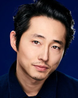 Studio portrait headshot of a dark-haired man with light facial hair against a deep blue background
