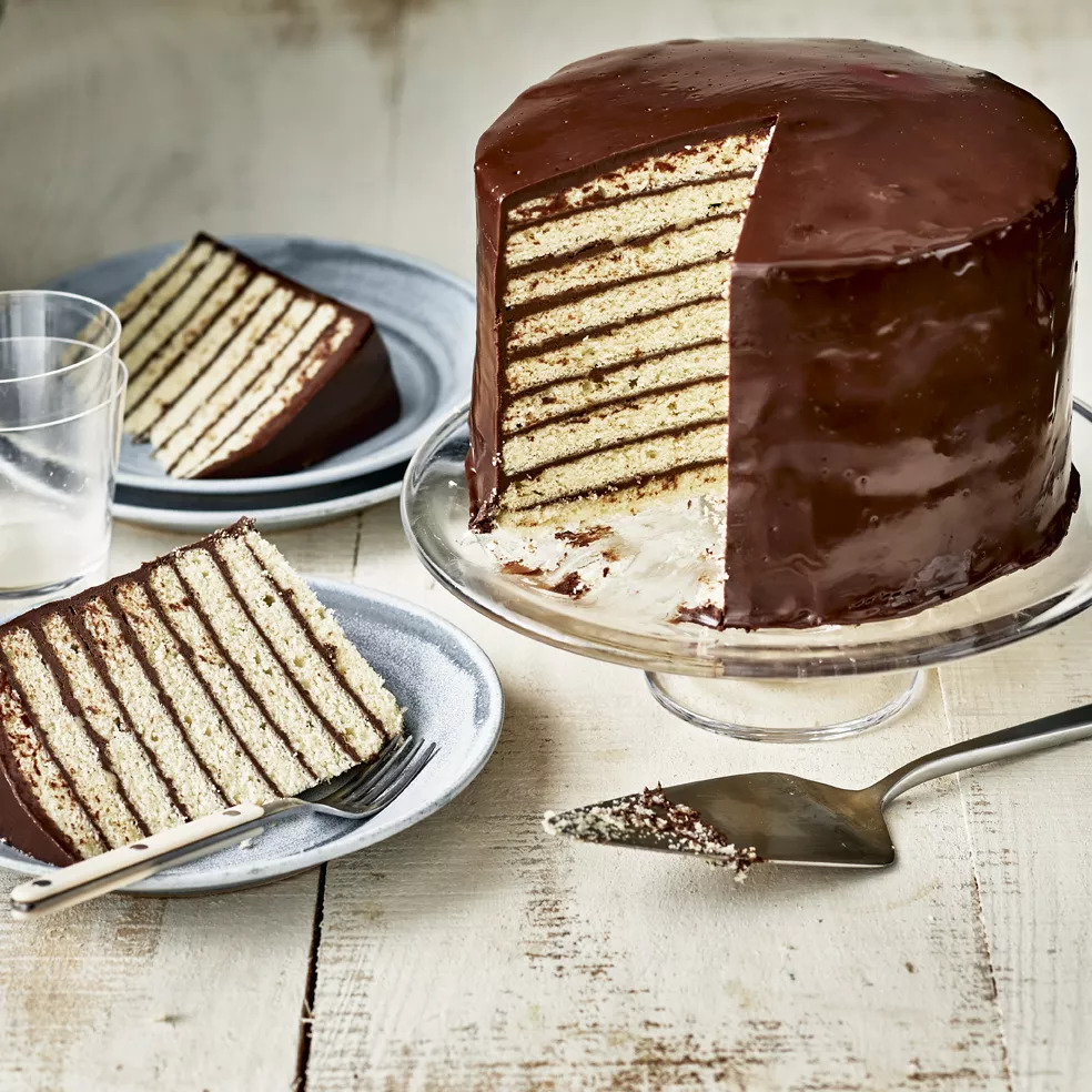 Tall layered chocolate cake with multiple thin yellow layers and dark chocolate frosting, slice cut to show interior