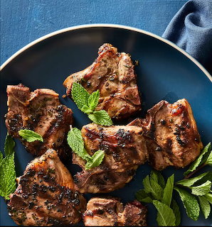 Grilled lamb chops on a dark plate with fresh mint leaves