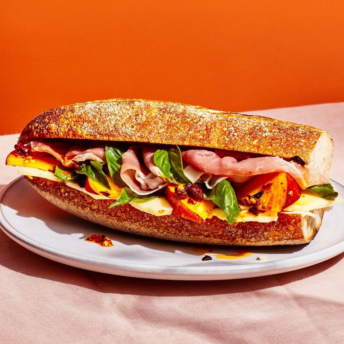 Artisan sandwich with prosciutto, peach, greens and peppers on seeded bread