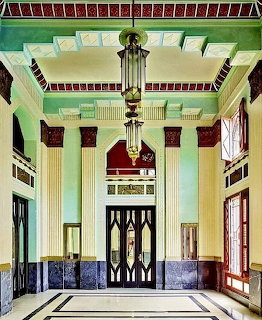 Art Deco lobby interior with mint green walls, ornate ceiling, and central geometric elevator doors