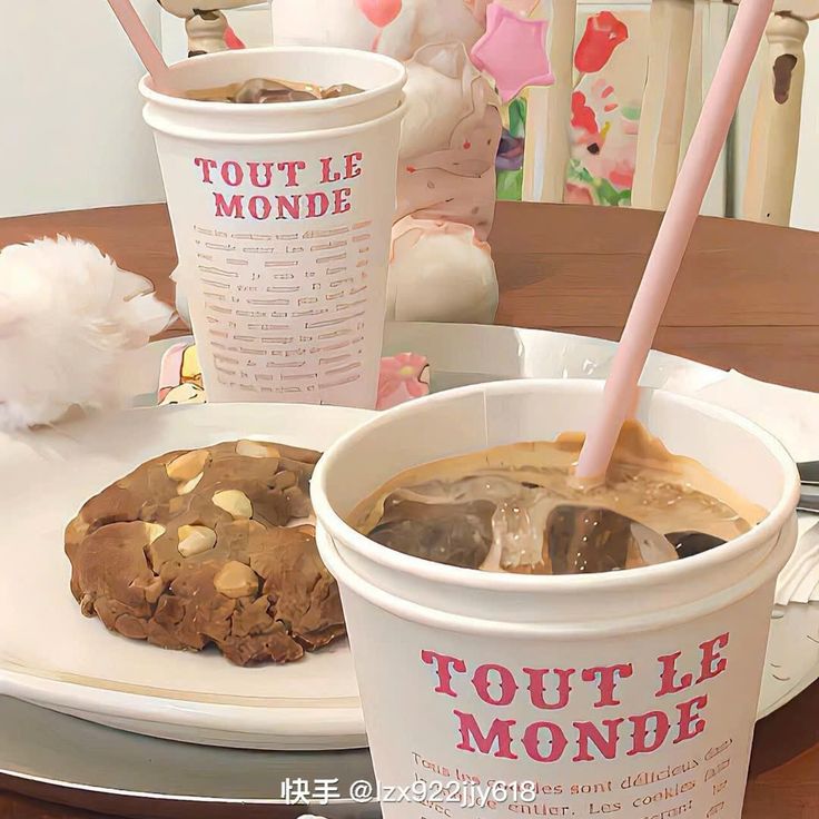 Two Tout Le Monde coffee cups with a chocolate chip cookie on a white plate